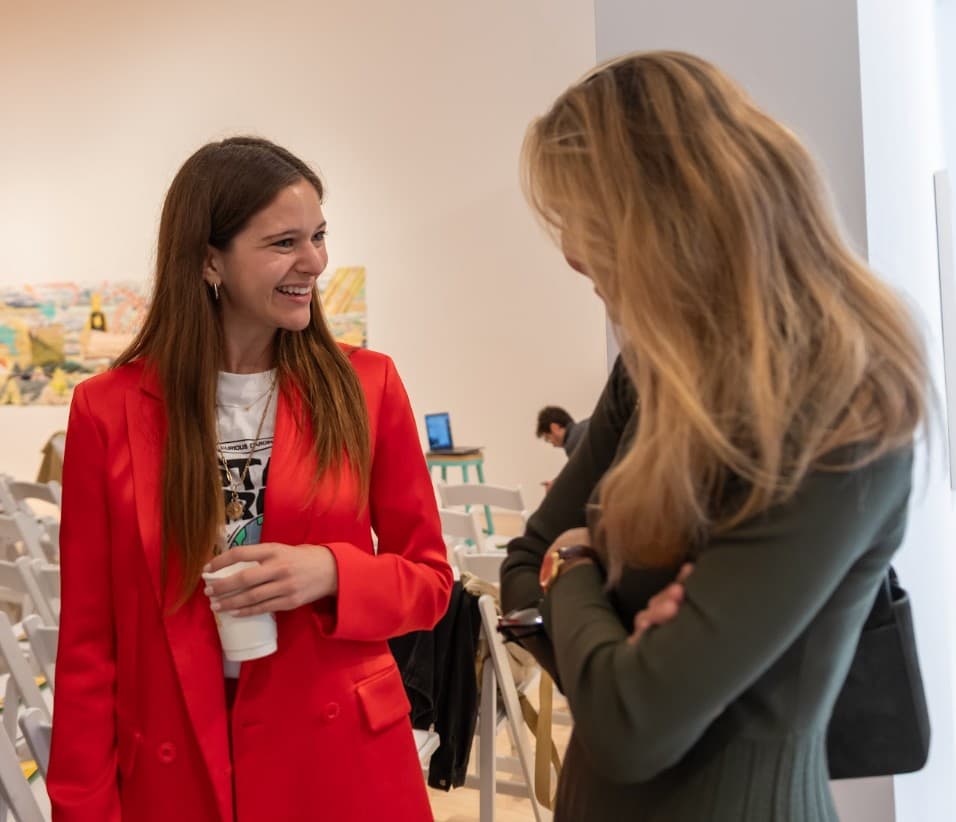 A community member in a red blazer chatting with an attendee at an event.