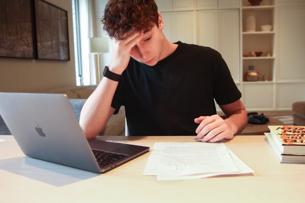 Student looking overwhelmed at a desk with a graded paper and laptop